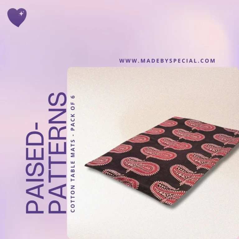 A set of handcrafted cotton table mats featuring red paisley block prints on a dark brown background. Displayed with soft lighting on a pastel pink and beige gradient backdrop. Text reads “PaiseD-Patterns – Cotton Table Mats, Pack of 6”